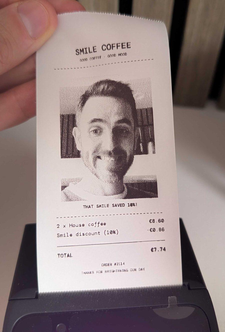 A thermal receipt from Smile Coffee coming out of the printer, with a dithered black and white photo of a grinning customer, 2 house coffees, a 10% smile discount and a total of €7.74