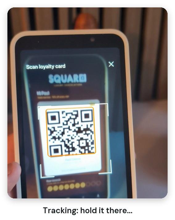 An S700 scanning a QR code on a phone, with an amber box around the code while it tracks